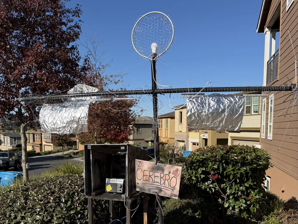 The Cerebro antenna rig in daylight: a steel mast with a dish on top, a control box on a stand, and a hand-lettered CEREBRO sign.