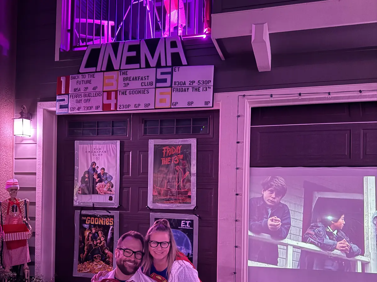 A cinema front built onto a garage, its marquee and movie posters lit pink, with a couple posing out front.