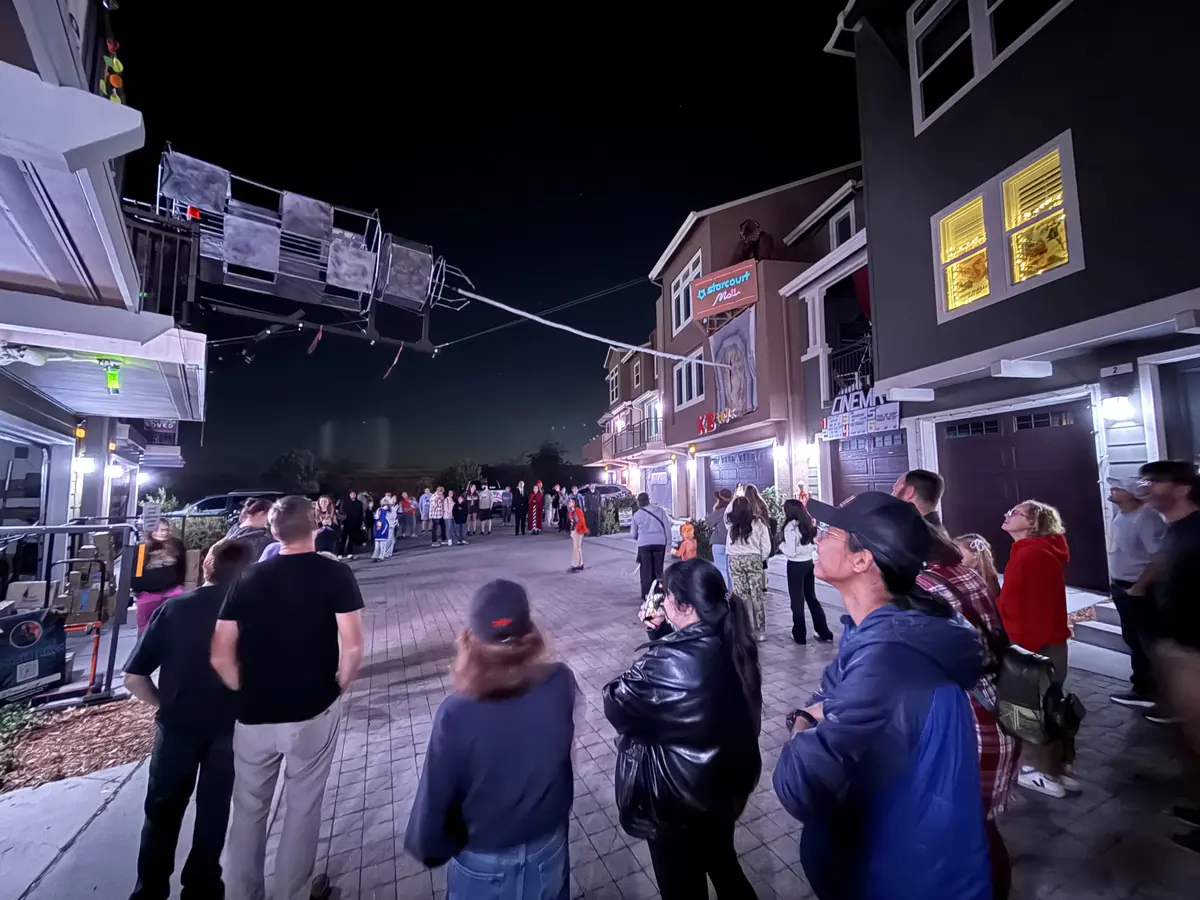 Visitors standing in the street at night, looking up at the rig strung overhead between the houses.