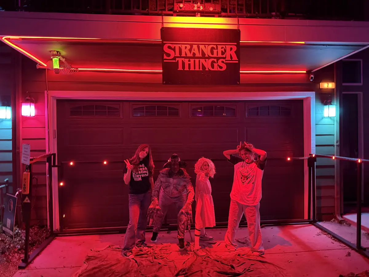 Four people in costume, one of them a Demogorgon, posing in front of a red-lit garage under a Stranger Things sign.