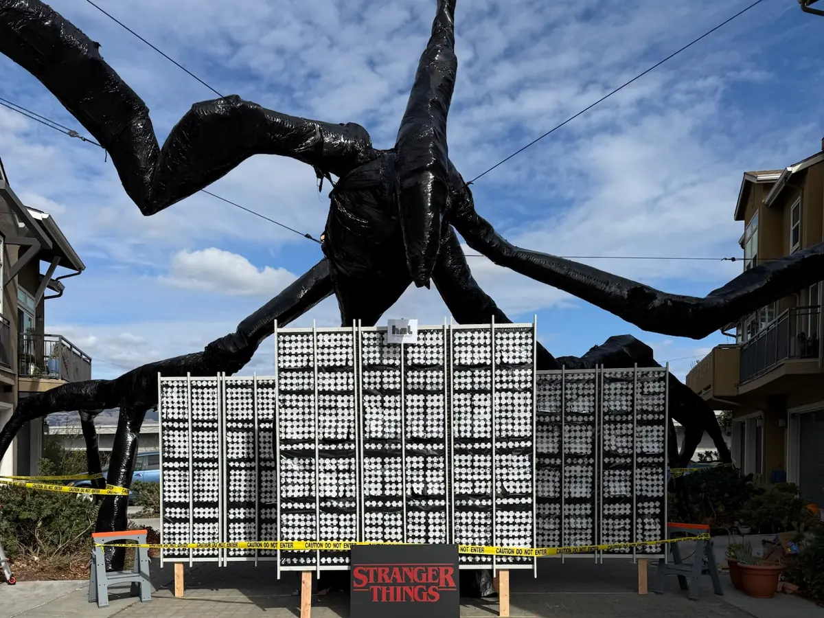 The giant Mind Flayer sculpture in daylight, its legs spread over the panel wall and the Stranger Things sign below.