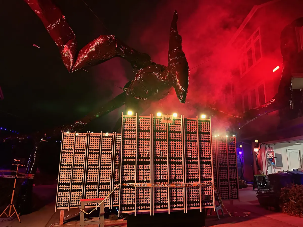 A giant black Mind Flayer sculpture reaching over a wall of lit panels, red haze and fog behind it.