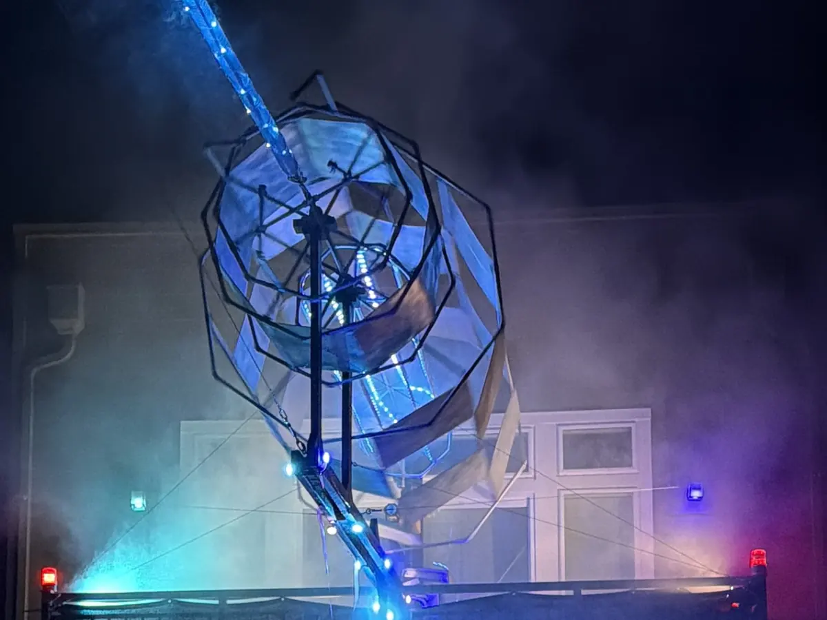 A huge wireframe portal sculpture angled above a balcony, wrapped in fog and lit blue from within, a beam of light shooting out of it.
