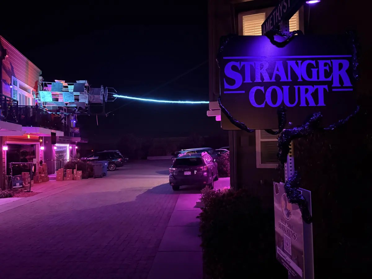 The purple Stranger Court street sign glowing at night, with the lit-up cul-de-sac and the overhead rig behind it.