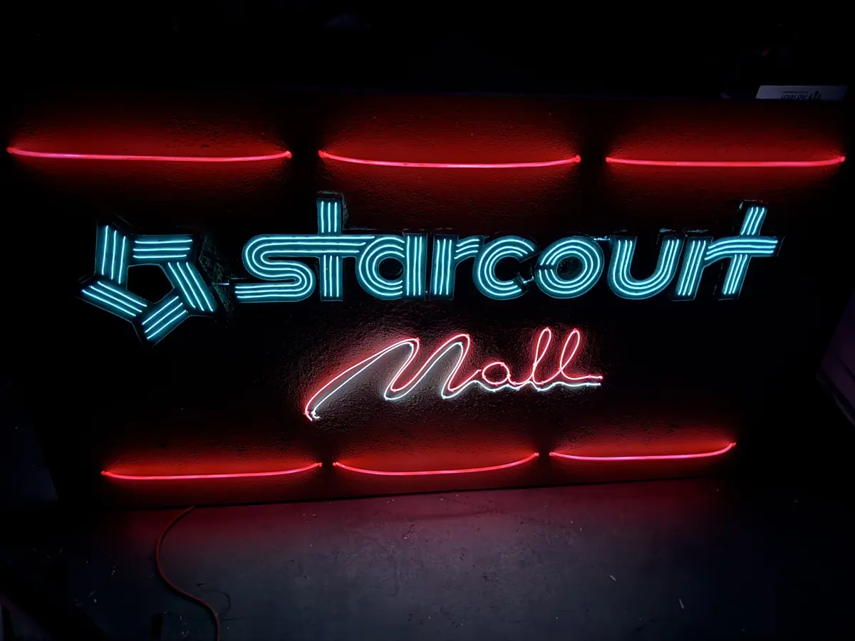 A neon-style Starcourt Mall sign glowing teal and red in the dark.