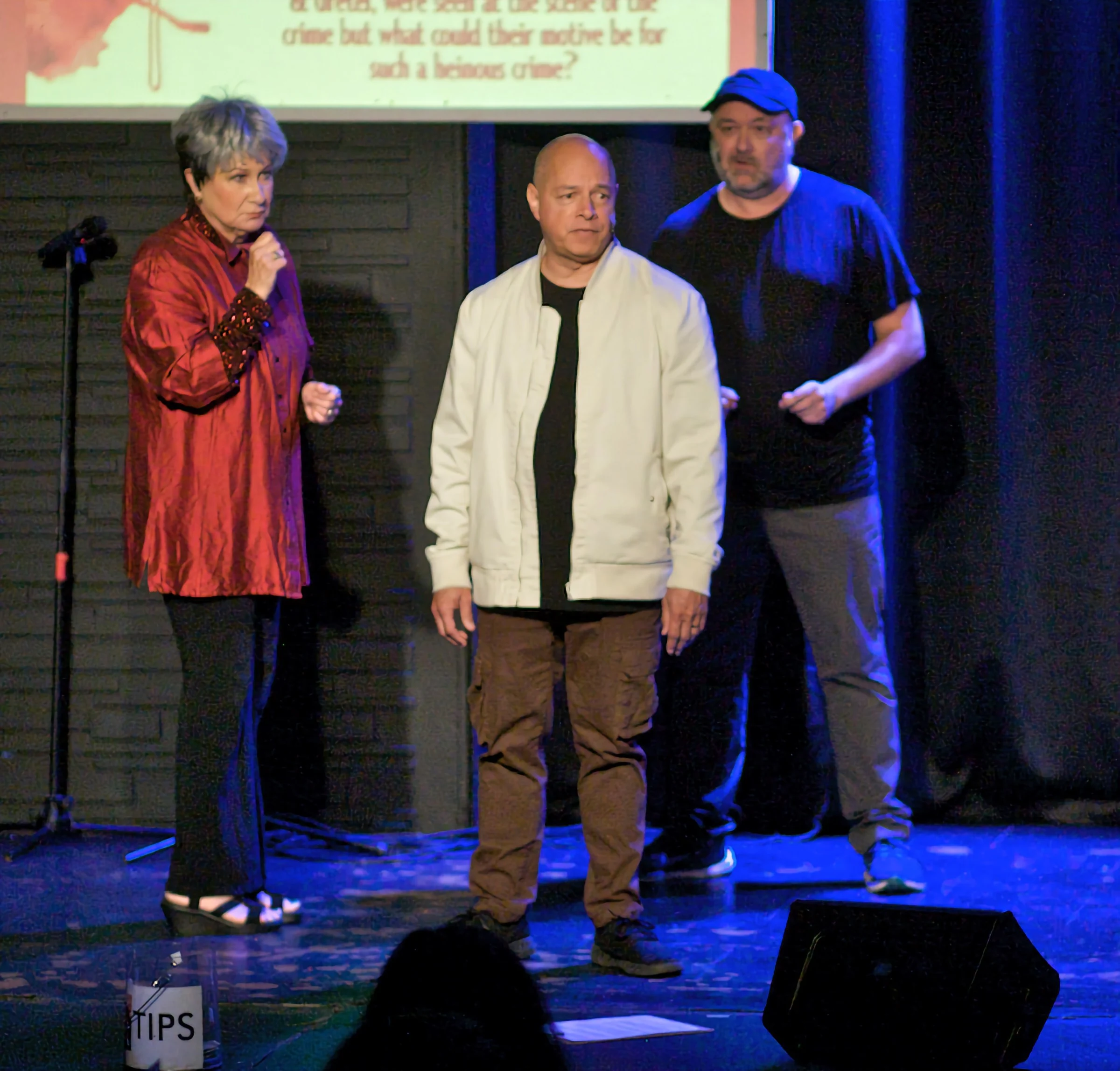 Cheryl King onstage with a microphone beside two improvisers mid-scene